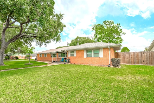 back of property with a lawn, fence, and brick siding