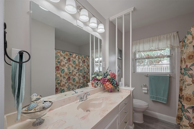 bathroom with vanity, baseboards, toilet, and a wealth of natural light