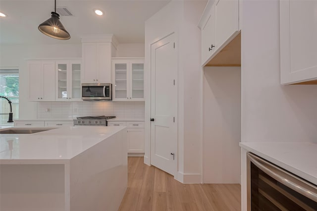 kitchen with decorative backsplash, appliances with stainless steel finishes, a sink, light countertops, and light wood-style flooring