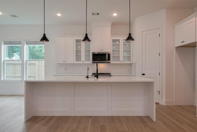 kitchen with visible vents, stainless steel microwave, white cabinets, light wood-style flooring, and backsplash
