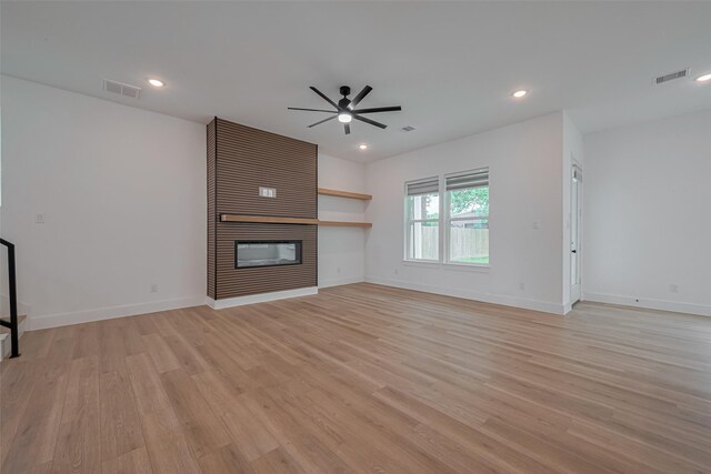 unfurnished living room featuring ceiling fan, visible vents, a large fireplace, and light wood finished floors