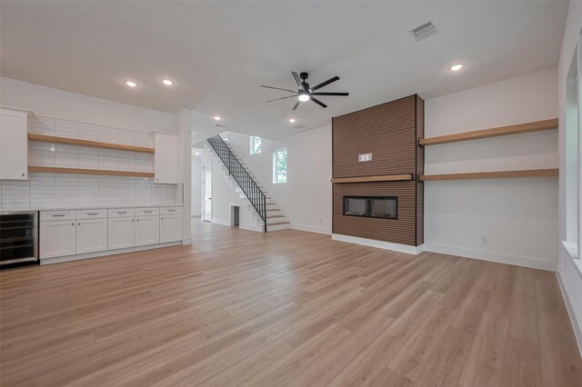 unfurnished living room featuring a fireplace, beverage cooler, baseboards, a ceiling fan, and light wood-style flooring
