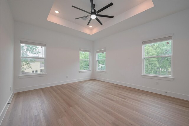 spare room featuring a healthy amount of sunlight, a raised ceiling, ceiling fan, and light wood-style flooring