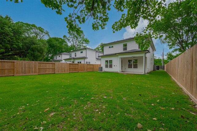 back of property with a fenced backyard, central AC unit, ceiling fan, and a yard