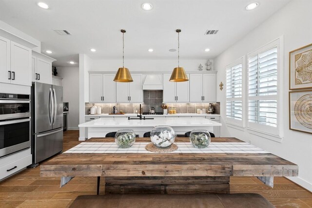 kitchen with light countertops, a kitchen island with sink, stainless steel appliances, and dark wood finished floors