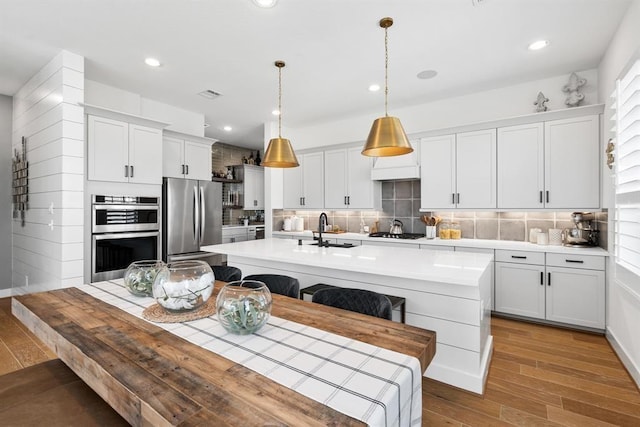 kitchen with appliances with stainless steel finishes, a sink, light wood-style floors, light countertops, and a center island with sink