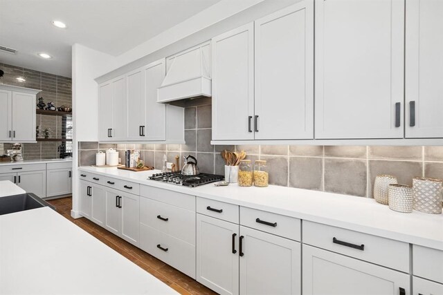 kitchen featuring custom exhaust hood, recessed lighting, light countertops, white cabinetry, and tasteful backsplash
