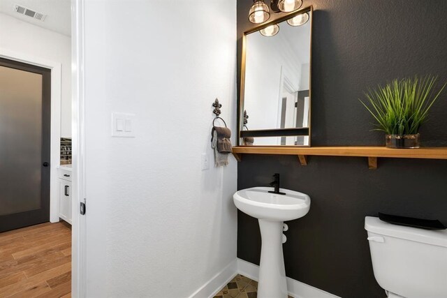 half bath with visible vents, baseboards, wood finished floors, and toilet