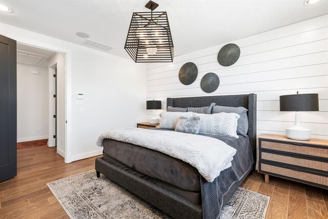 bedroom with wood walls, recessed lighting, baseboards, wood finished floors, and visible vents