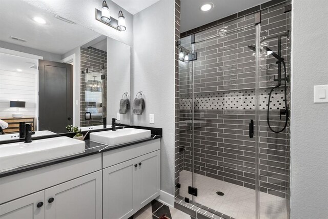 bathroom with a sink, a stall shower, double vanity, and visible vents