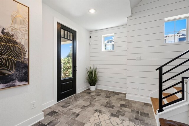 entryway featuring baseboards, wood walls, brick patterned floor, and stairway