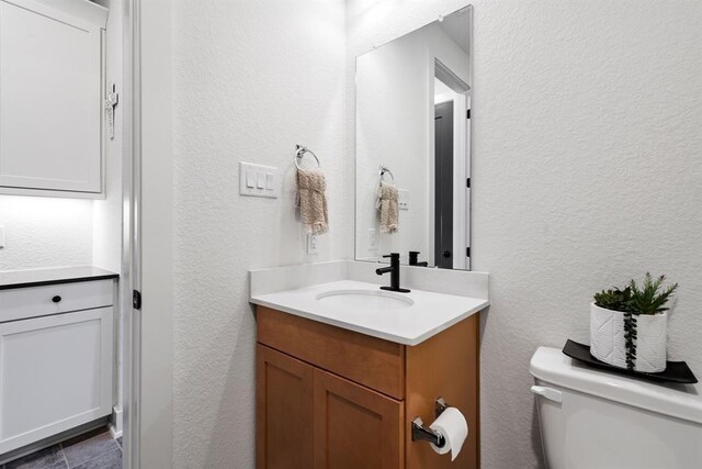 half bath with vanity, a textured wall, and toilet