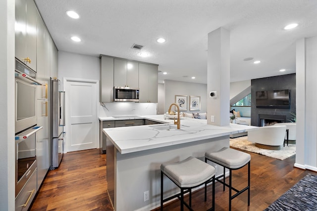 kitchen featuring stainless steel appliances, gray cabinets, a sink, light stone counters, and a peninsula