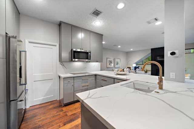 kitchen featuring gray cabinets, stainless steel appliances, a sink, dark wood-type flooring, and light stone countertops