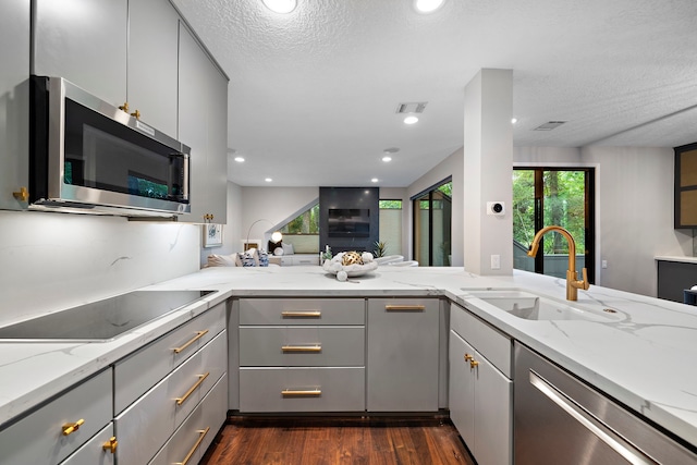 kitchen with gray cabinetry, stainless steel appliances, a sink, dark wood-type flooring, and light stone counters