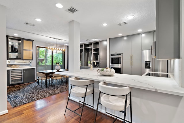 kitchen featuring wine cooler, stainless steel double oven, a peninsula, light stone countertops, and recessed lighting