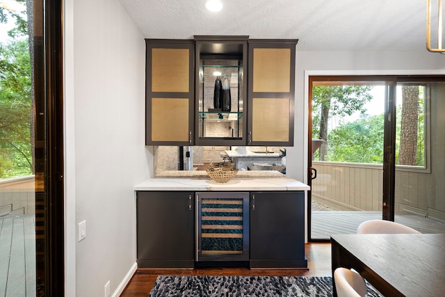 indoor bar featuring wine cooler, dark wood finished floors, a textured ceiling, and baseboards