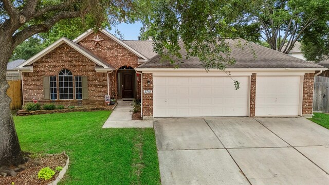 ranch-style home with roof with shingles, an attached garage, a front lawn, brick siding, and driveway