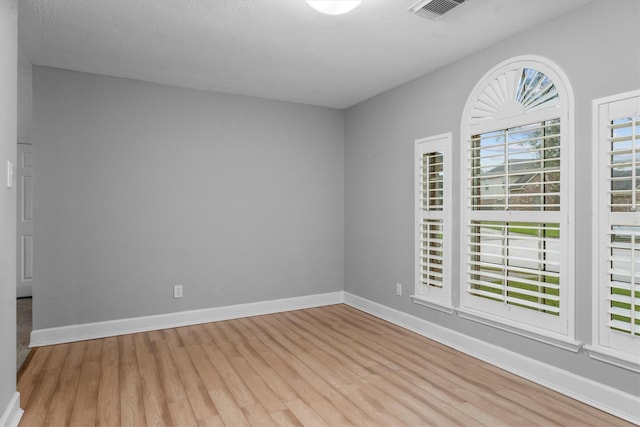 unfurnished room featuring baseboards, light wood-style flooring, and visible vents
