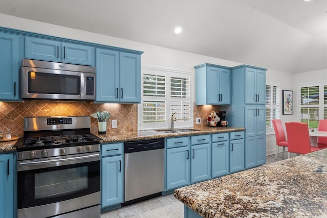 kitchen with dark stone counters, stainless steel appliances, a sink, backsplash, and blue cabinetry