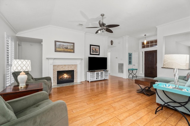 living area with visible vents, ornamental molding, ceiling fan, a fireplace with flush hearth, and light wood finished floors