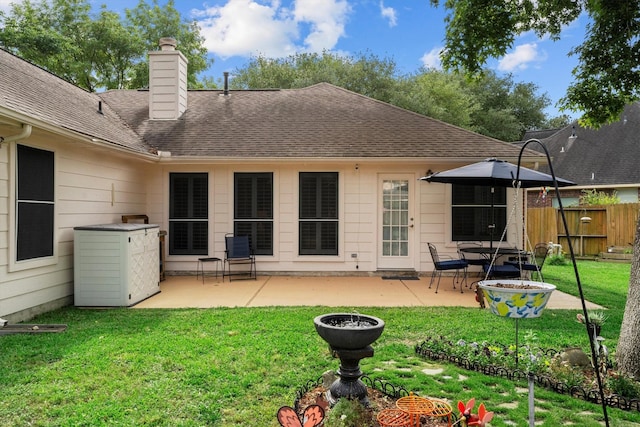 back of property with a chimney, roof with shingles, a lawn, a patio area, and fence