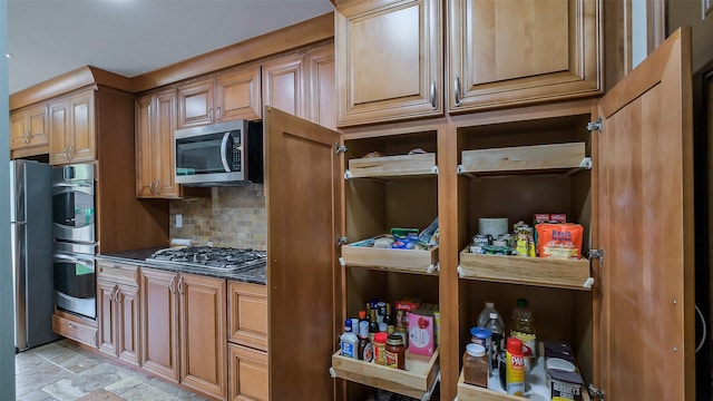 kitchen with dark stone counters, decorative backsplash, stone finish floor, and stainless steel appliances