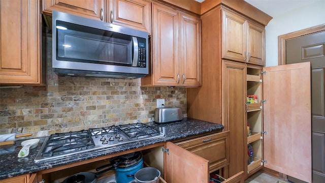 kitchen with backsplash, appliances with stainless steel finishes, brown cabinetry, and dark stone counters