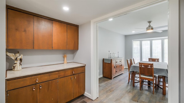 kitchen with brown cabinetry, wood finished floors, recessed lighting, light countertops, and a ceiling fan