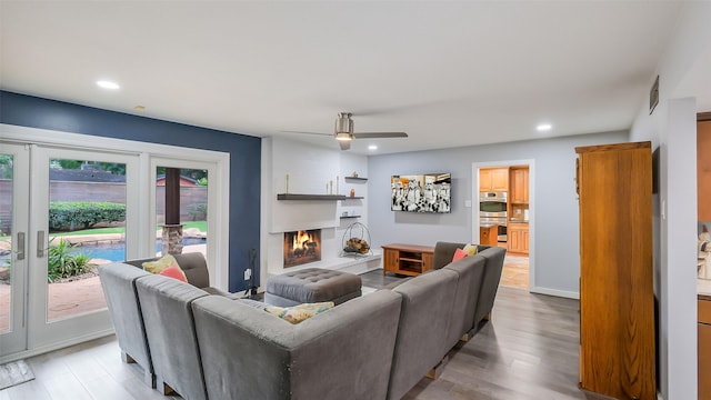 living room featuring recessed lighting, light wood finished floors, a ceiling fan, and a warm lit fireplace