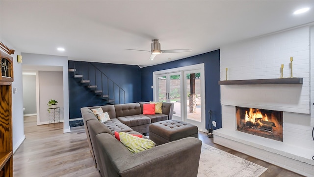 living area with a brick fireplace, a ceiling fan, recessed lighting, wood finished floors, and stairway