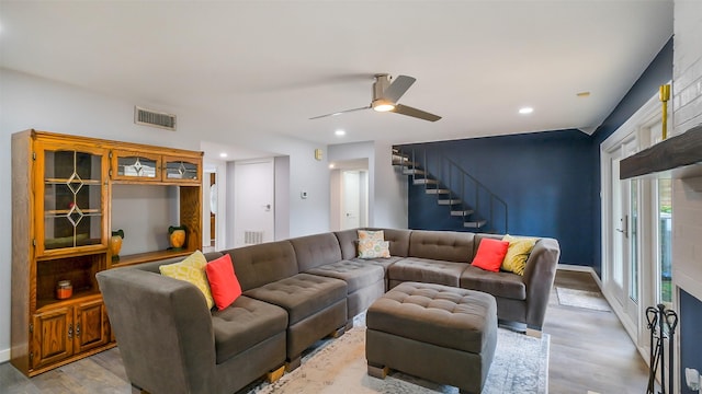 living area with stairs, a ceiling fan, visible vents, and light wood finished floors