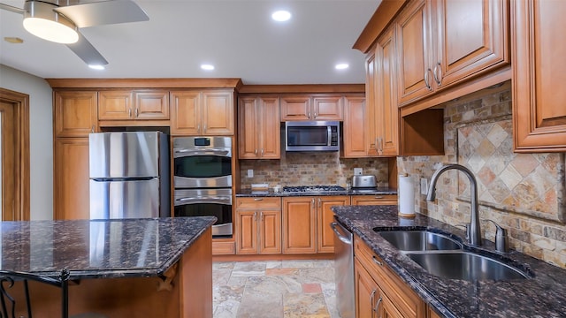 kitchen with stone finish floor, appliances with stainless steel finishes, a sink, and dark stone counters