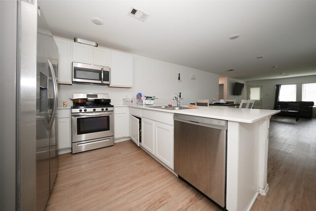 kitchen featuring visible vents, a peninsula, light wood-type flooring, a sink, and appliances with stainless steel finishes