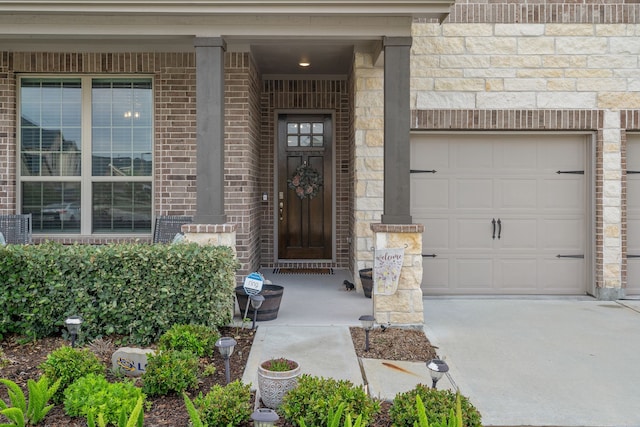 view of exterior entry with covered porch, stone siding, brick siding, an attached garage, and driveway