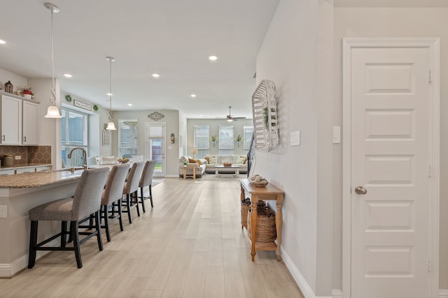 kitchen featuring white cabinets, a kitchen breakfast bar, decorative backsplash, and light wood-style floors