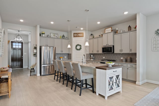 kitchen with gray cabinets, a sink, light wood finished floors, a breakfast bar, and stainless steel appliances