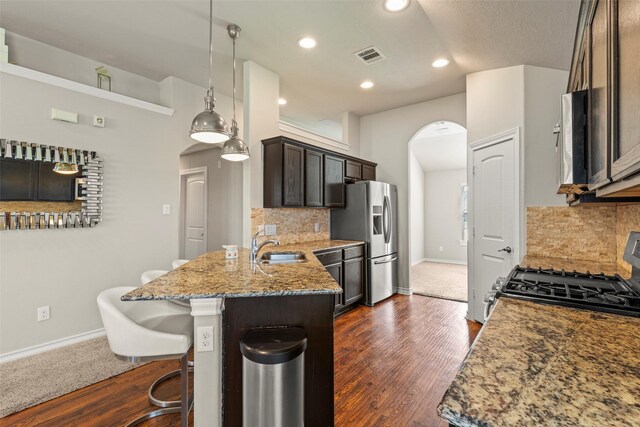 kitchen featuring appliances with stainless steel finishes, arched walkways, light stone countertops, a sink, and baseboards