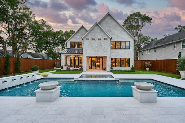 back of house at dusk with a yard, a standing seam roof, brick siding, a patio area, and a fenced backyard