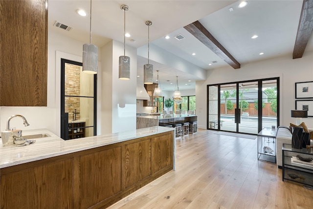 kitchen with beamed ceiling, light stone counters, visible vents, and a sink