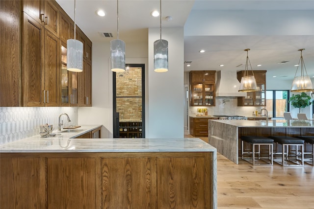 kitchen featuring custom exhaust hood, visible vents, a sink, tasteful backsplash, and light wood-type flooring