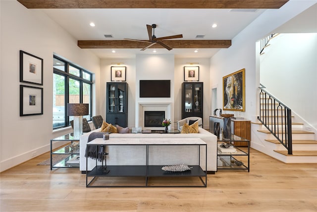 living area featuring ceiling fan, stairs, beamed ceiling, and light wood-style floors