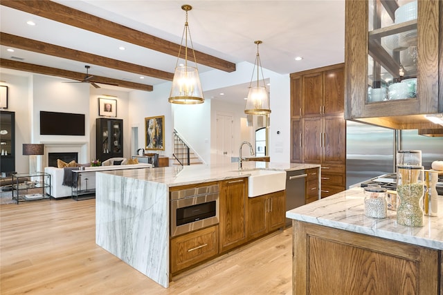 kitchen featuring appliances with stainless steel finishes, a spacious island, light wood finished floors, a sink, and beam ceiling