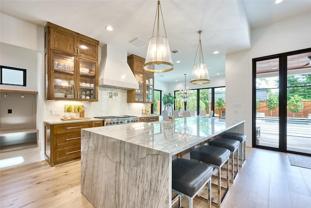 kitchen featuring brown cabinetry, light wood-style floors, a large island, and custom range hood