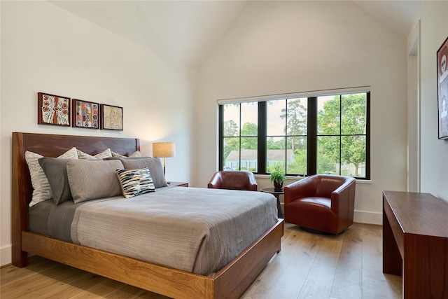 bedroom featuring light wood finished floors, multiple windows, and high vaulted ceiling
