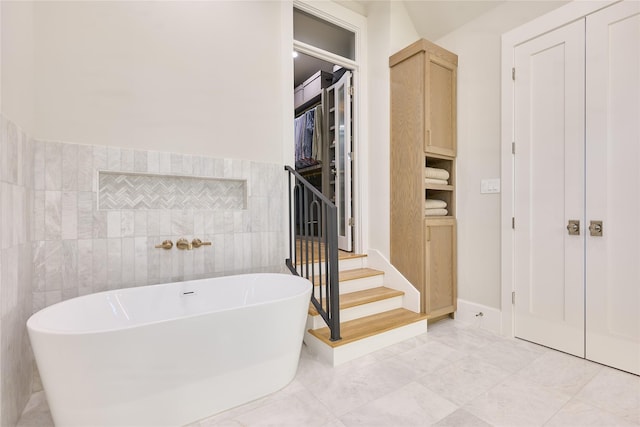 bathroom with tile walls, a closet, marble finish floor, a soaking tub, and a wainscoted wall