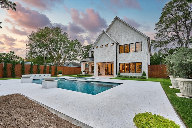 pool at dusk featuring a patio, an in ground hot tub, a fenced backyard, and a fenced in pool