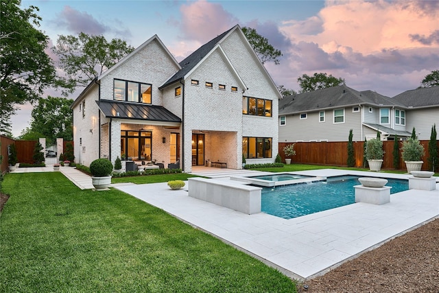 back of house at dusk with an in ground hot tub, a lawn, a fenced backyard, brick siding, and a patio area