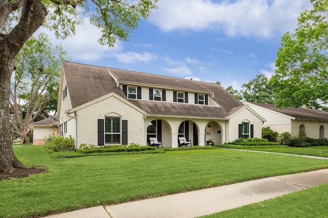 view of front of home featuring a porch, brick siding, roof with shingles, and a front yard
