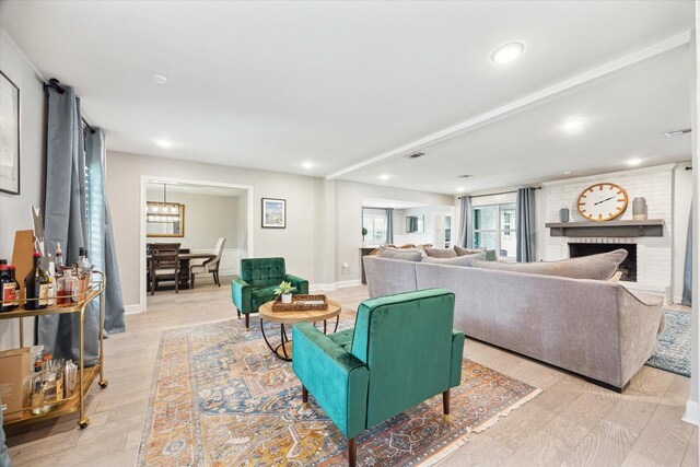 living area with visible vents, light wood-style flooring, a brick fireplace, and baseboards